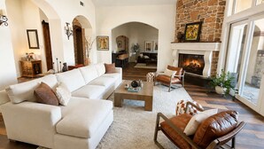 A spacious living room with a white sofa, leather armchair, and a fireplace. - Luxury Temecula Estate Pool Spa Views Theater (Temecula)