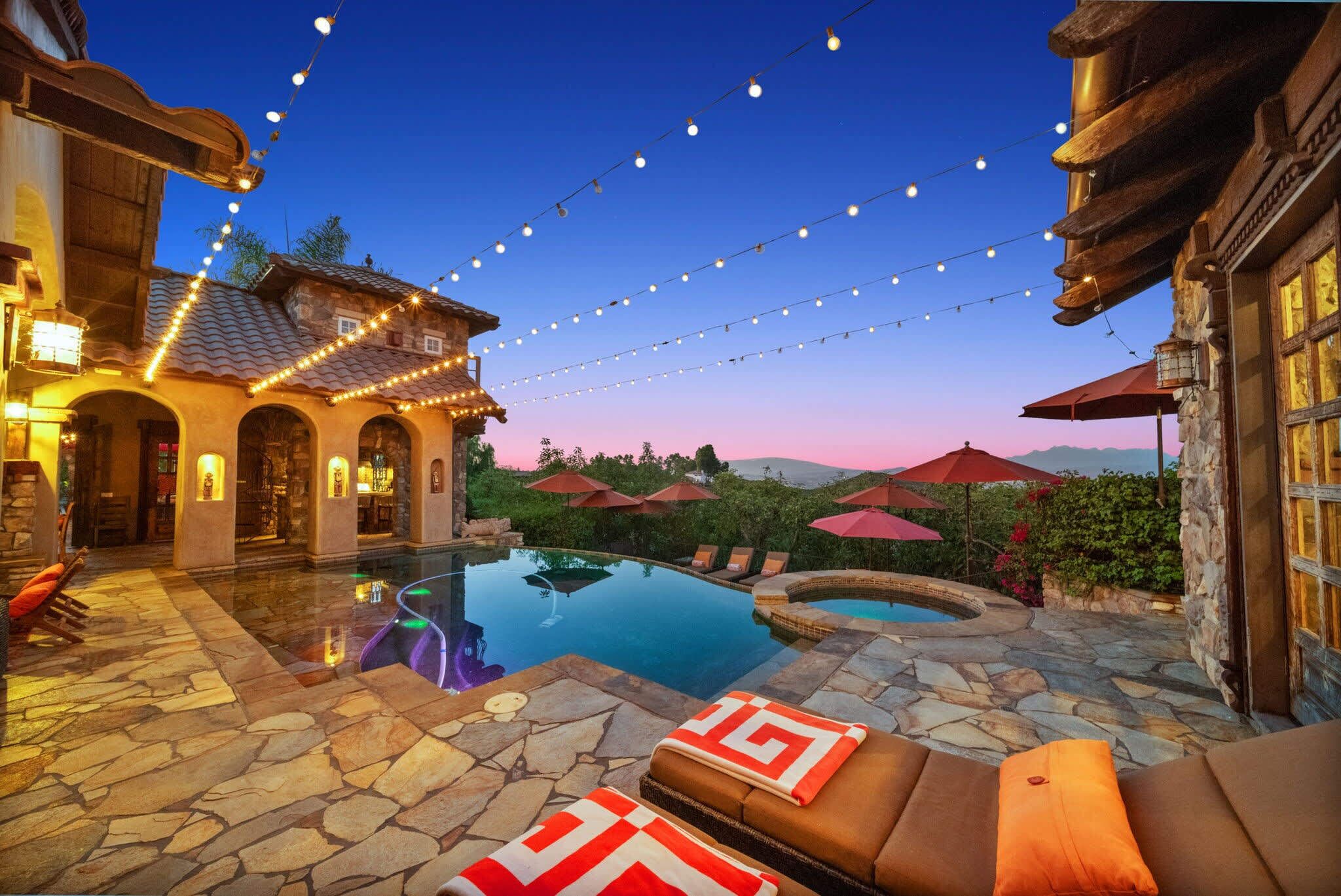 A pool area with stone flooring, lounge chairs, and string lights.
