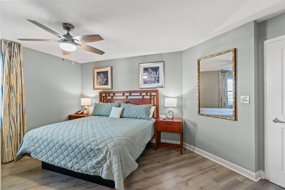 A bedroom with a bed, a nightstand, a lamp, a ceiling fan, and a mirror.