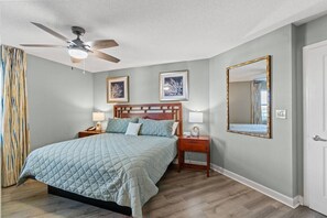 A bedroom with a bed, a nightstand, a lamp, a ceiling fan, and a mirror. - Oceanfront Dunes Village - Lazy River & Waterpark! (Myrtle Beach)