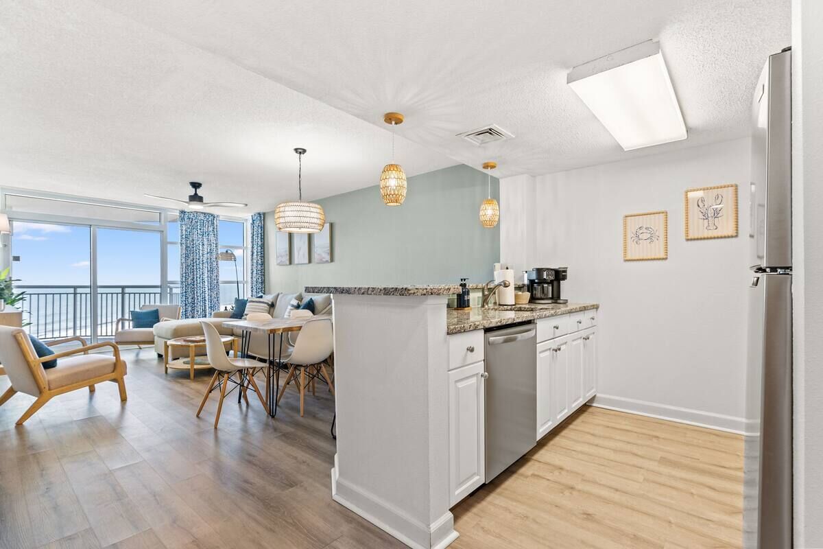 Una cocina moderna con una isla central, muebles blancos e iluminación colgante.