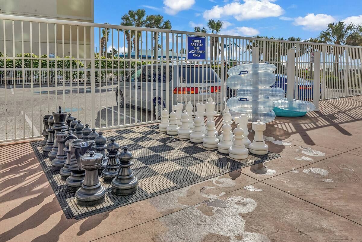 A chessboard with chess pieces arranged on a patterned mat, a parking area with a white fence, and a sign indicating tubes are for the Lazy River only.
