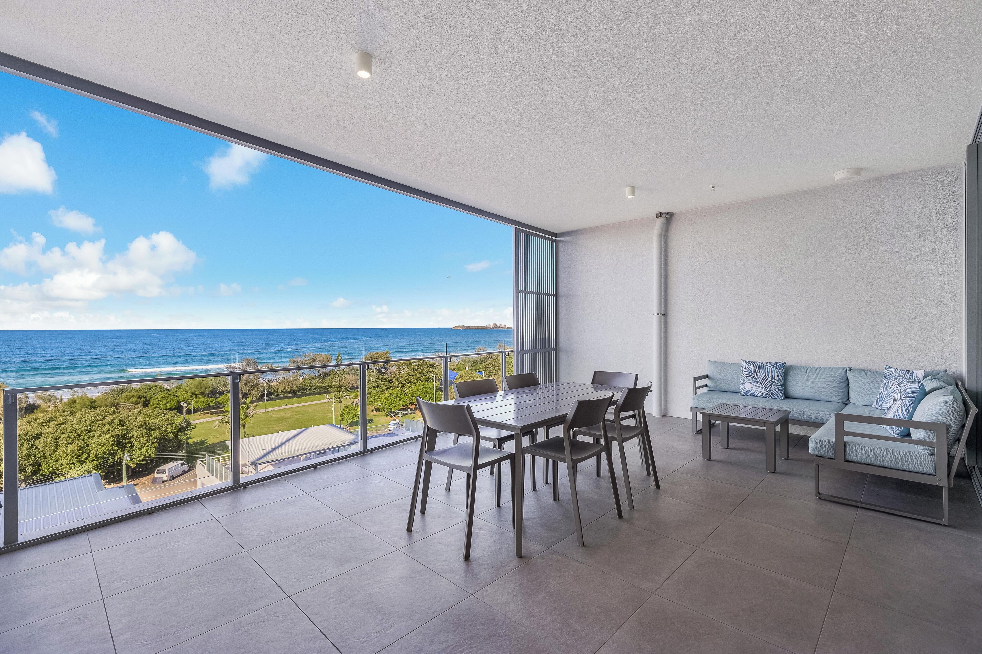 A spacious balcony with a clear view of the ocean, a dining table with chairs, and a sofa with patterned cushions.
