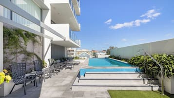 Un espace piscine avec des chaises longues et un ciel d’un bleu éclatant.