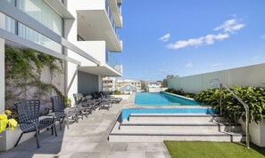 Un área de piscina con sillones reclinables y un cielo azul despejado.