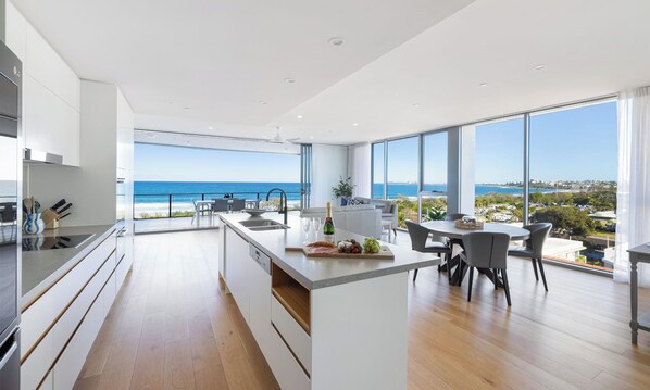 A modern kitchen with a large island, a dining area with a view of the ocean, and a spacious living area with large windows.