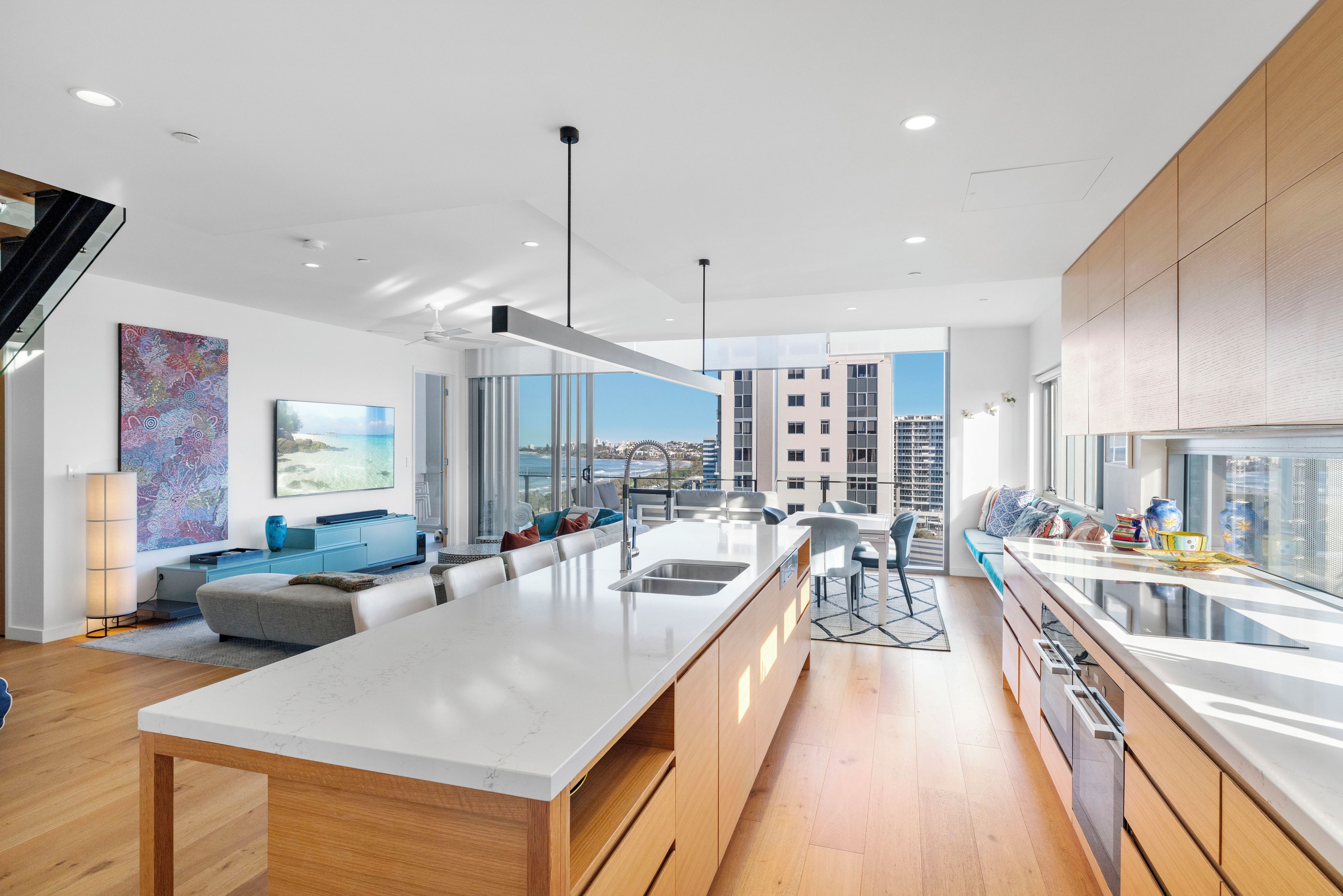 Una cocina moderna con una isla central, un comedor con vistas y una sala de estar con sofá y obras de arte.
