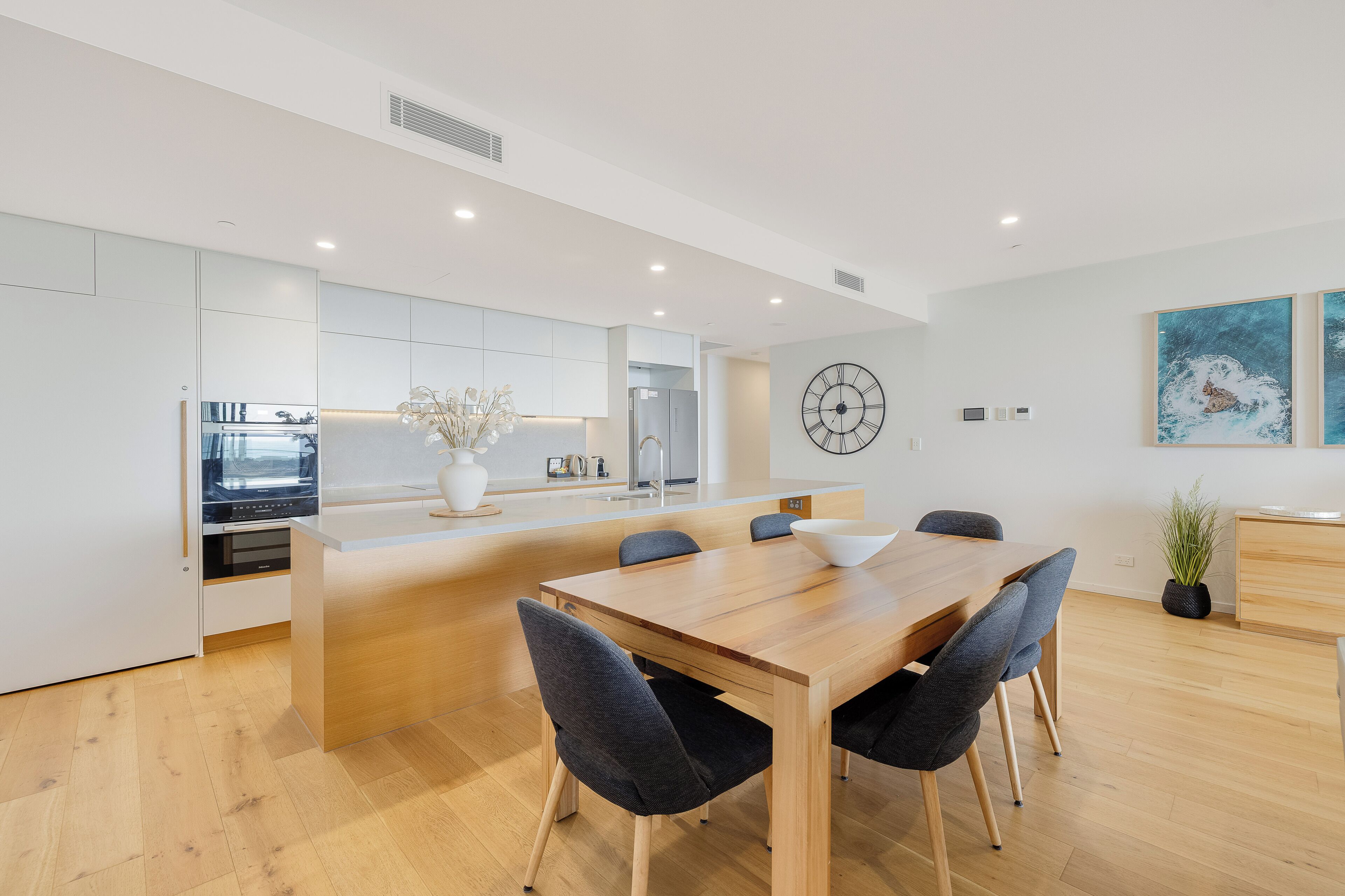 A modern kitchen with white cabinets, a central island, and a dining area with a wooden table and chairs.