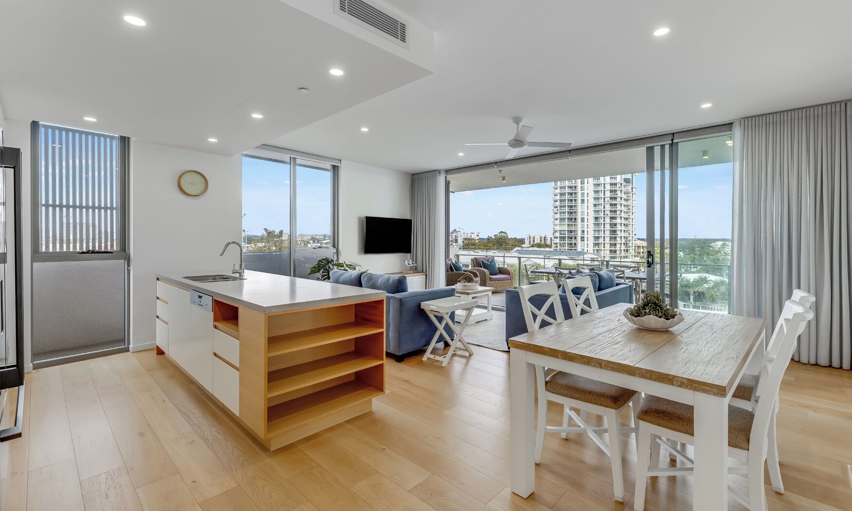 A modern apartment with a kitchen, dining area, and living space with large windows and a city view.