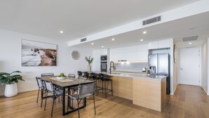 Una cocina moderna con una isla central, un comedor con mesa y sillas de madera, y un amplio ventanal con vista al mar.