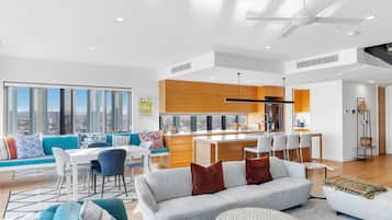 Una sala moderna con sofá, mesa de comedor y sillas, una cocina con armarios de madera y un ventanal con vistas a la ciudad.