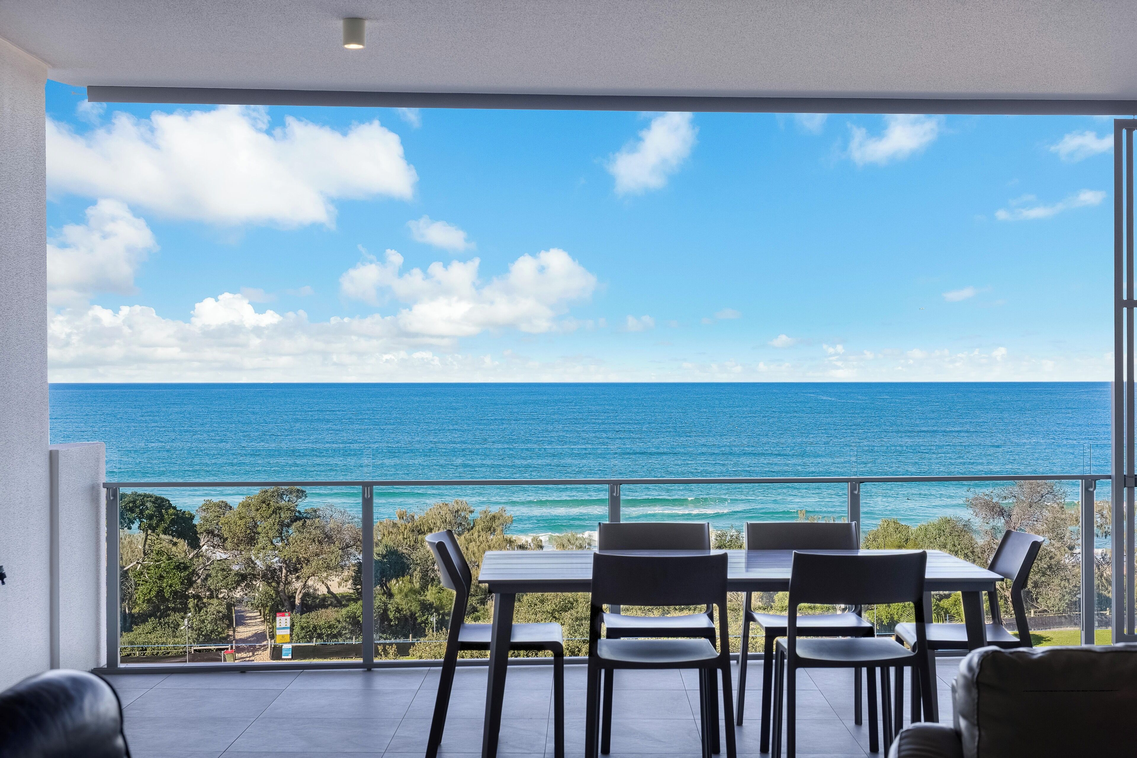 A balcony with a table and chairs overlooking a clear blue sea and sky.