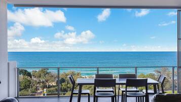 A balcony with a table and chairs overlooking a clear blue sea and sky.