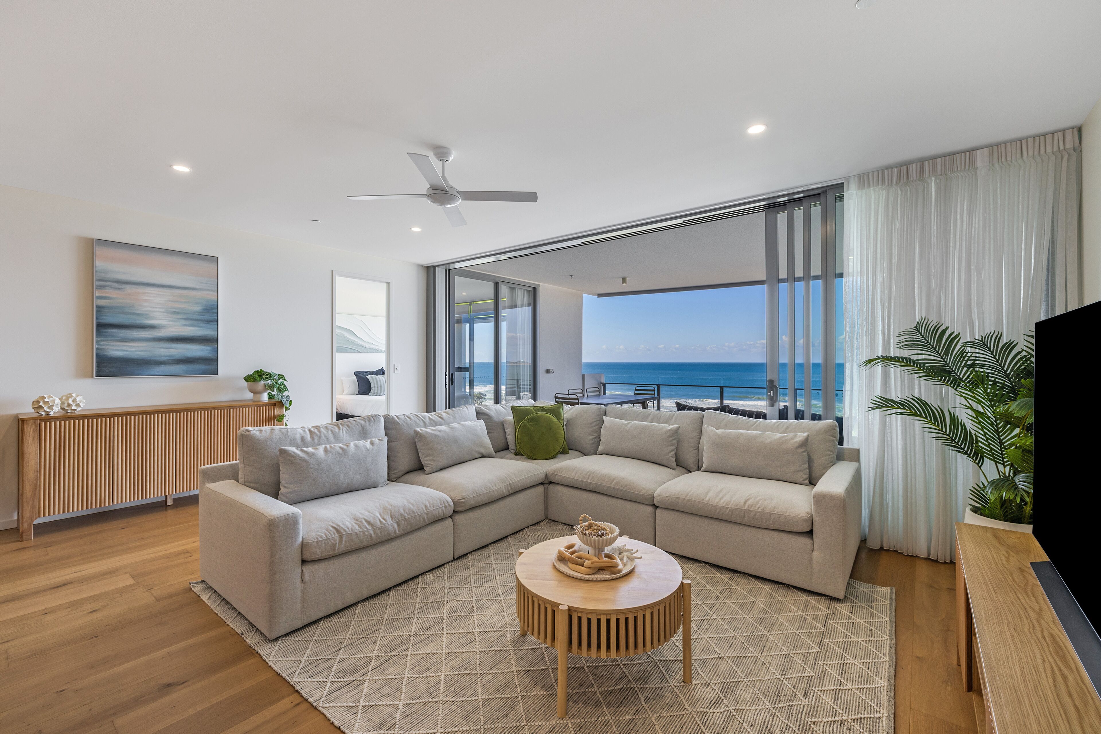 Uma sala de estar moderna com um amplo sofá de canto, uma mesa de centro redonda e vista para o mar.