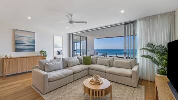 Uma sala de estar moderna com um amplo sofá de canto, uma mesa de centro redonda e vista para o mar.