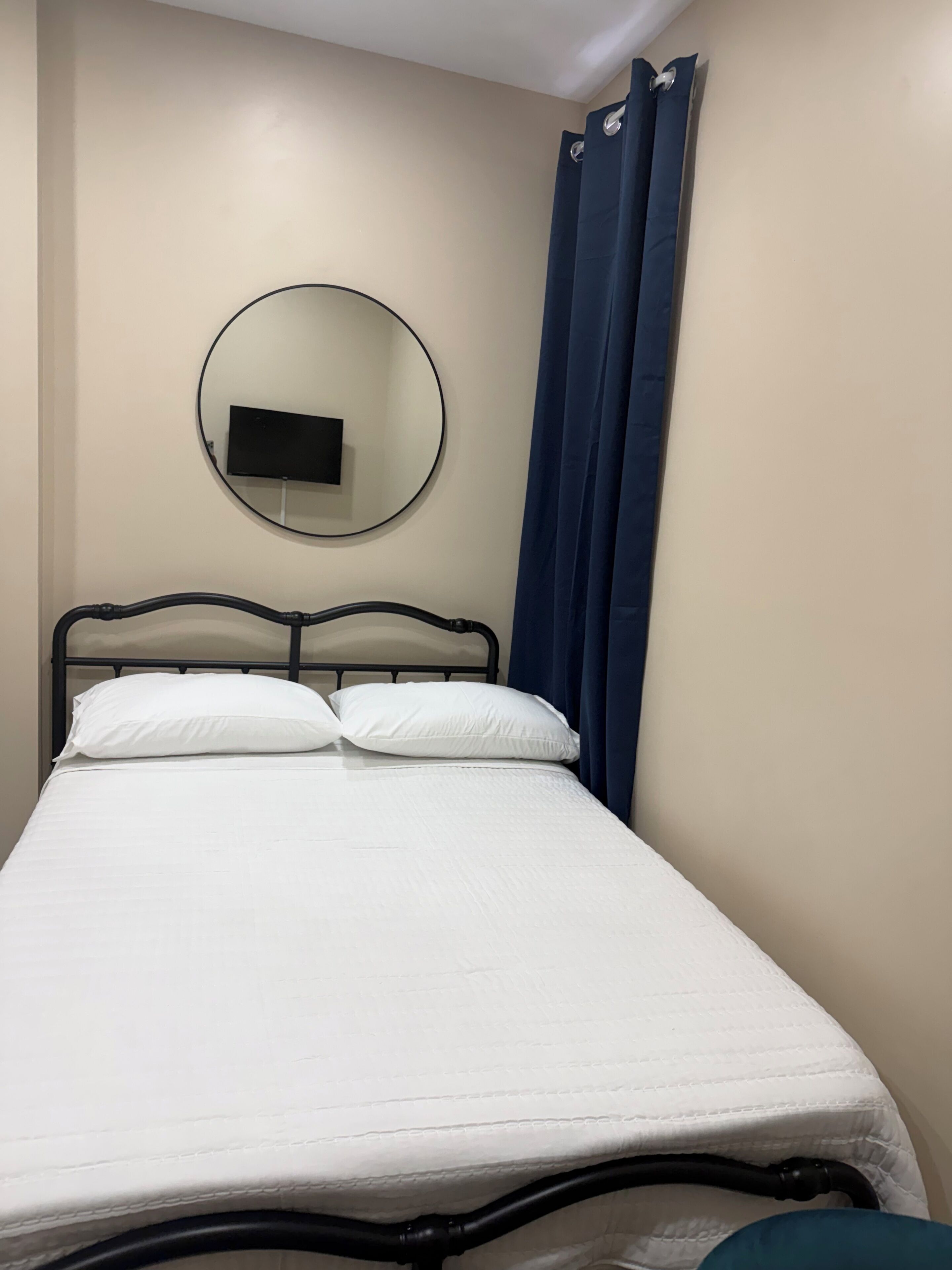 Una cama con cabecera, un televisor instalado en la pared y una cortina azul.