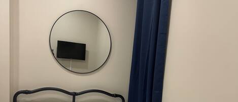 Una cama con cabecera, un televisor instalado en la pared y una cortina azul.