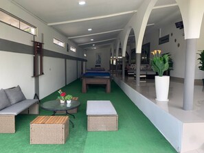 A pool table in a room with green artificial turf, a sofa, a small table with flowers, and a potted plant.