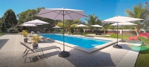 A swimming pool with lounge chairs and umbrellas, surrounded by palm trees and a clear sky.