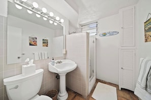 A bathroom with a toilet, sink, and mirror with lights, a shower, and a towel rack. - Oceanfront 1BR, Waikīkī's Gold Coast, Diamond Head (Honolulu)