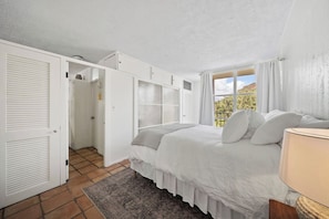 A bedroom with a bed, a nightstand, a window with curtains, and a view of the outdoors. - Oceanfront 1BR, Waikīkī's Gold Coast, Diamond Head (Honolulu)