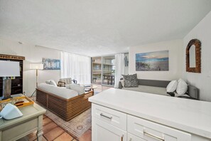A modern living room with a sofa, a coffee table, and a dining area. There is a large window with curtains, a painting on the wall, and a sign that reads 'YPSY PALACE'. - Oceanfront 1BR, Waikīkī's Gold Coast, Diamond Head (Honolulu)