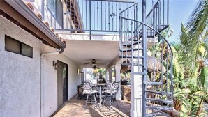 A covered patio with a spiral staircase, outdoor seating, and a view of a tropical garden. - Moana Del Sol - Vineyard Estate + Resort Pool (Temecula)