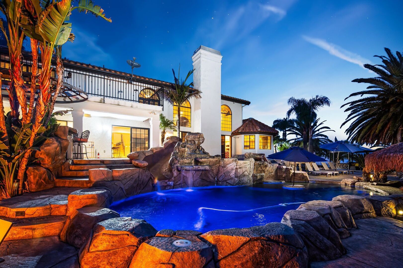 Un resort con piscina, piante tropicali e un edificio bianco con ampie finestre.
