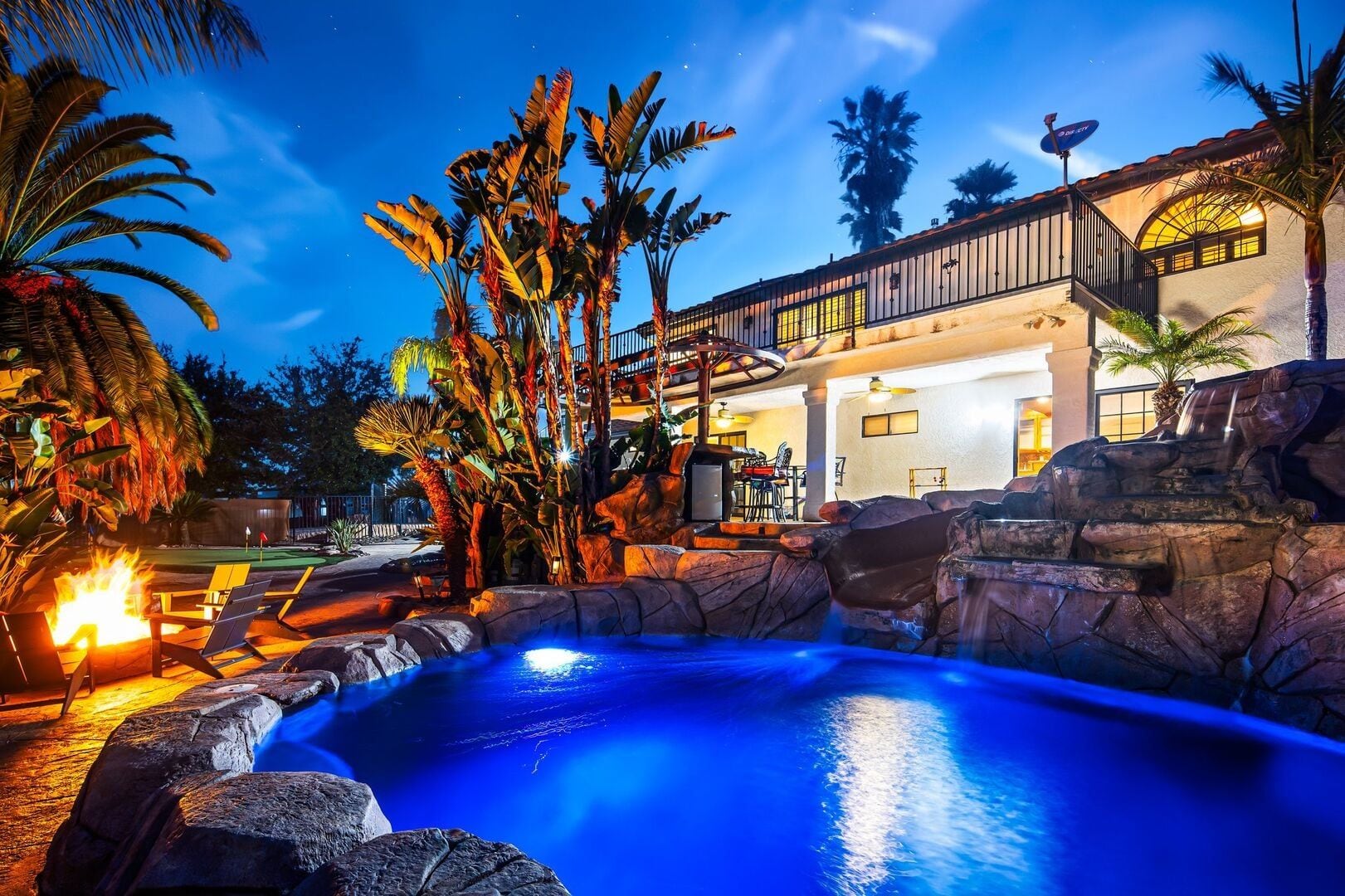 A pool with a waterfall, surrounded by tropical plants and a building with a balcony.