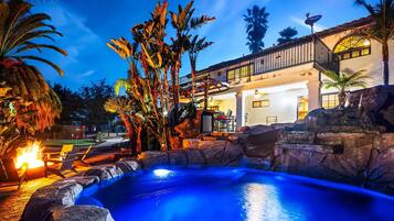 A pool with a waterfall, surrounded by tropical plants and a building with a balcony.