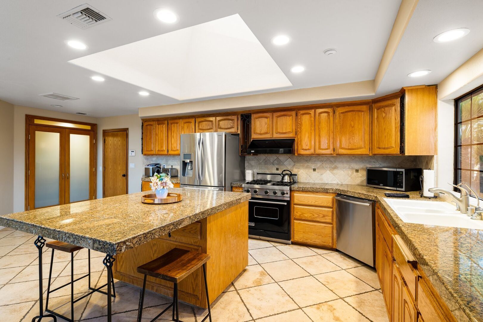 A kitchen with granite countertops, wooden cabinets, stainless steel appliances, and a central island with stools.