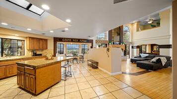A spacious kitchen with a central island, a dining area with chairs, and a living area with a sofa.