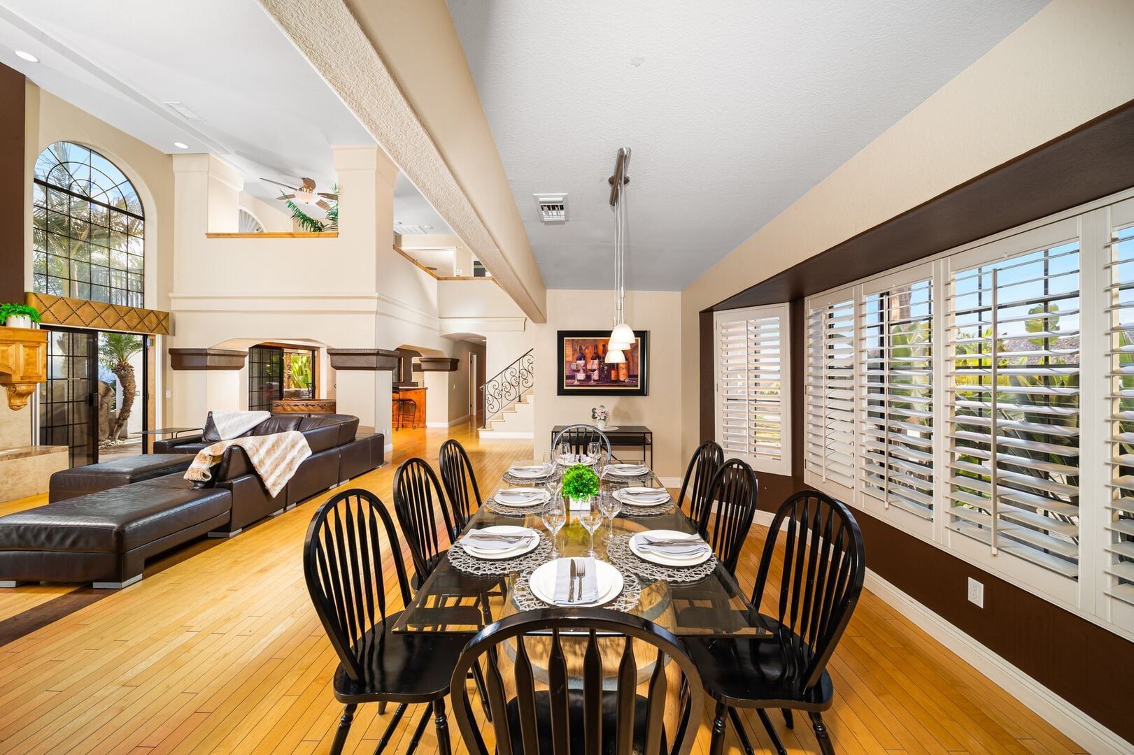A spacious dining area with a long table set for six, surrounded by black chairs, in a modern interior with wooden flooring and large windows.
