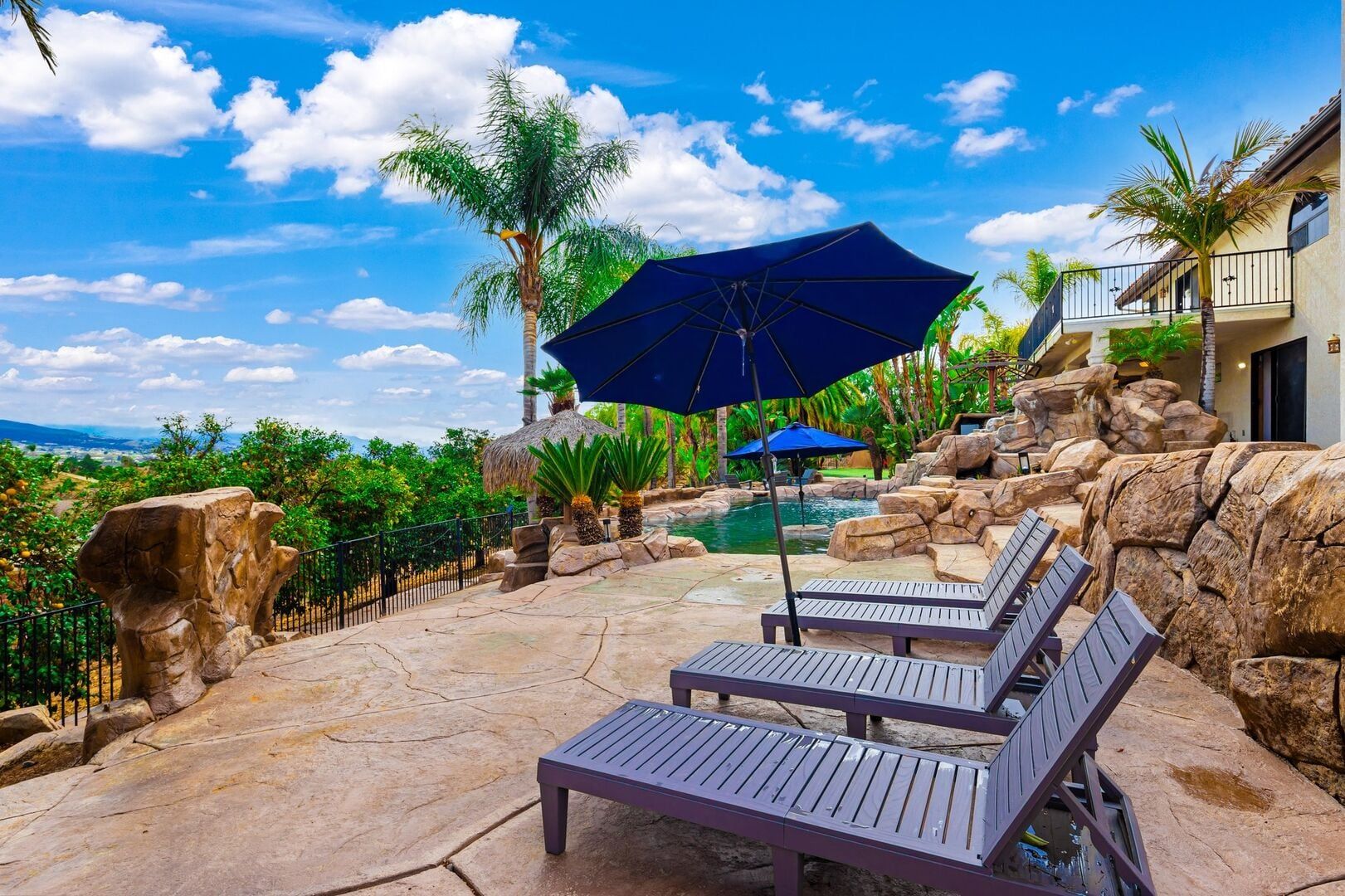 A poolside area with lounge chairs and umbrellas, surrounded by tropical plants and a view of the landscape.