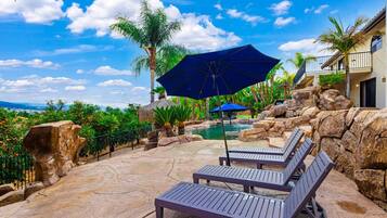 A poolside area with lounge chairs and umbrellas, surrounded by tropical plants and a view of the landscape.