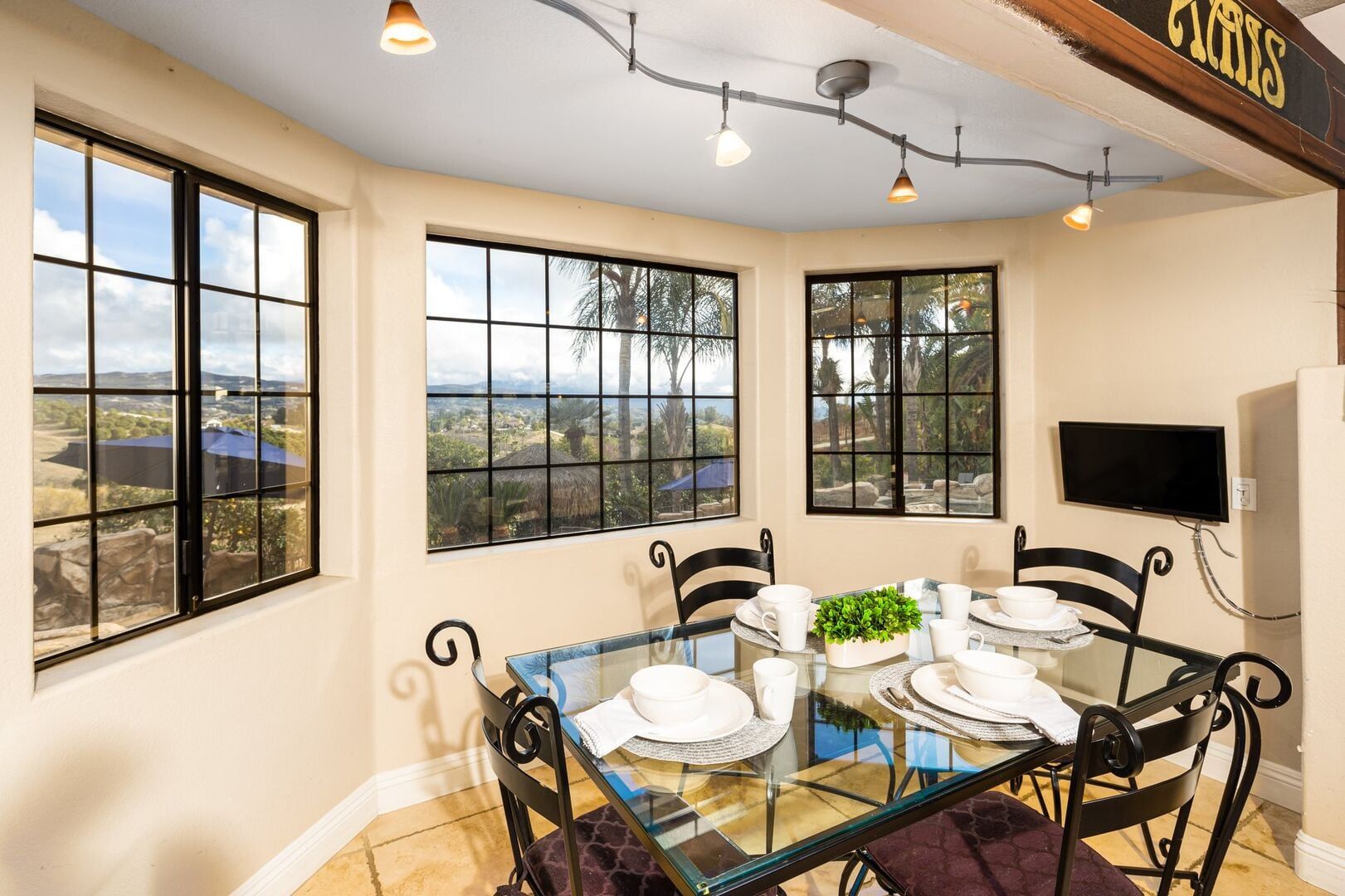 A dining area with a glass table, black chairs, and a view of a landscape through large windows.
