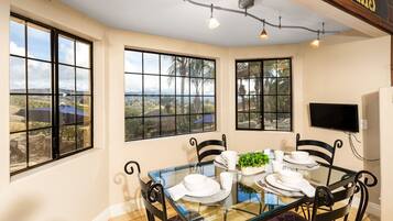 A dining area with a glass table, black chairs, and a view of a landscape through large windows.
