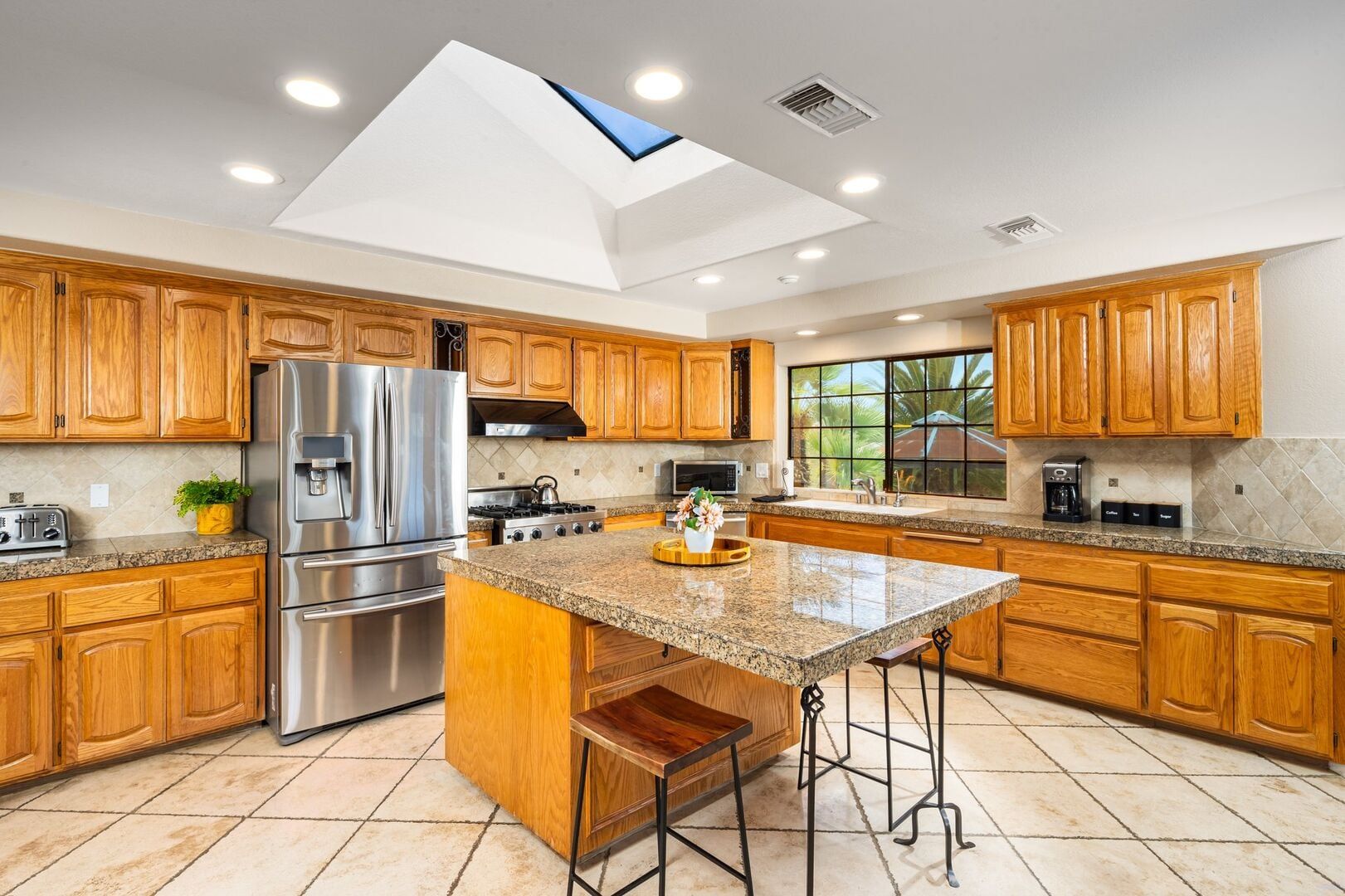 Et moderne køkken med træskabe, rustfrie stål-hvidevarer, en køkkenø med granitbordplade og et ovenlysvindue.