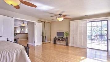 A spacious bedroom with a bed, a television on a stand, and a ceiling fan.