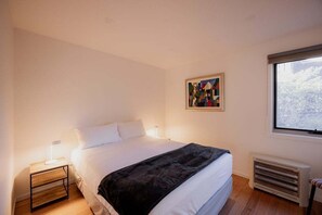 A bedroom with a bed, bedside table, lamp, radiator, and a window with a view. - Waterfront at Eggs and Bacon Bay "theshack@84" (Huon Valley)