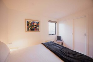 Ein Schlafzimmer mit einem Bett, einem Fenster, einem Sessel und einem Gemälde an der Wand.