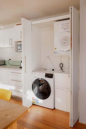 A compact laundry room with a washing machine, a dryer, and a small shelf. - Waterfront at Eggs and Bacon Bay "theshack@84" (Huon Valley)