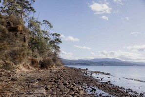 A rocky shoreline with trees and a distant view of mountains. - Waterfront at Eggs and Bacon Bay "theshack@84" (Huon Valley)