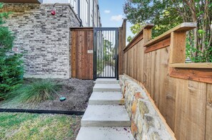 A narrow pathway leading to a gated entrance, flanked by a brick wall and a wooden fence. - Dallas Skyline Terrace Townhome (Dallas)