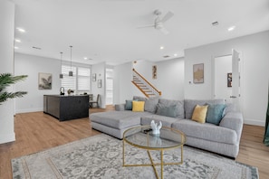 A modern living room with a grey sofa, a glass coffee table, and a kitchen area with a black countertop. - Dallas Skyline Terrace Townhome (Dallas)