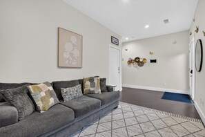 A modern living room with a grey sofa, patterned cushions, a geometric rug, a wall-mounted artwork, and a decorative wall piece. - Dallas Skyline Terrace Townhome (Dallas)
