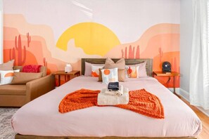 Ein Hotelzimmer mit einem Bett, einem Nachttisch, einem Sessel, einer Wandmalerei und einem Fenster mit Vorhängen.