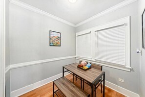 Ein Essbereich mit einem Holztisch und einer Bank, einem gerahmten Bild an der Wand und einem Fenster mit Jalousien.