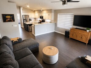 Un salon moderne avec un canapé d’angle gris, un pouf rond et un téléviseur posé sur un meuble en bois.