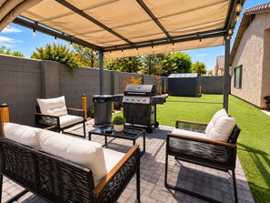 An outdoor patio area with a covered seating arrangement, a barbecue grill, and a trash bin. - Gilbert Oasis • Near Downtown Gilbert • King Suite • Private Yard & Grill (Gilbert)